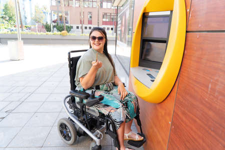 Disabled young woman in wheelchair with ATM