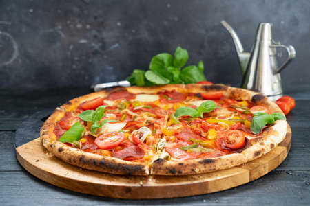 Pizza with salami and tomatoes on blak wooden tableの写真素材