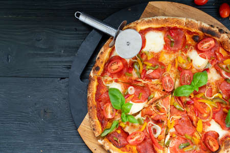 Pizza with salami and tomatoes top close up view on wooden tableの写真素材