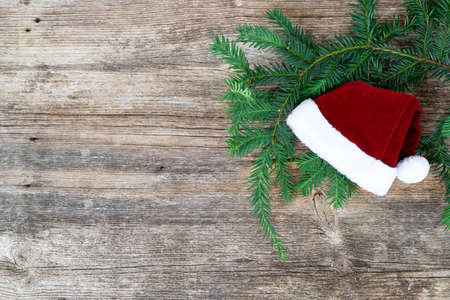 Rustic christmas lifestyle - evergreen twig decorated with santa claus hat on aged wooden backgroundの写真素材
