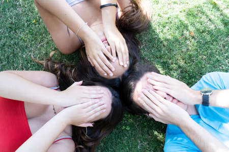Group of young happy people friends lying in circle on green grass in meadow and relaxing, closing eyes, teenagers spending time together outdoors on summer day, top viewの写真素材