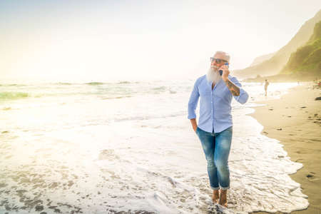 senior man talking on a phone on sea beach, distant online work and bussiness concept, senior people lifestyleの写真素材