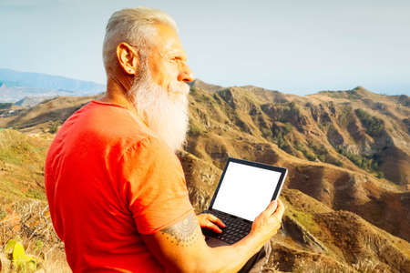 Senior man with laptop on the edge of a mountain with stunning views of the valley, healthy lifestyle and remote office conceptの写真素材