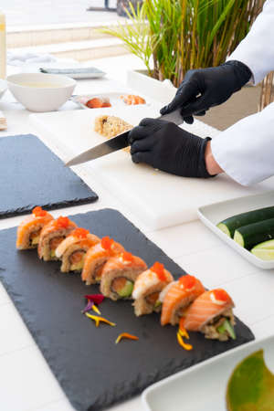 Making sushi. Cropped shot of professional chef in uniform peeling avocado, preparing ingredients for traditional japanese dish on kitchen table while working at outdoor beach restaurantの写真素材