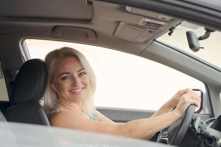 Happy smiling woman driving car and looking back, modern city life concept