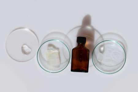 Glass petri dish with transparent pure serum for skin care with serum cosmetic bottle on white background, top view. Concept laboratory tests and research, making and testing cosmeticの写真素材