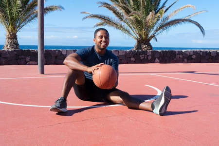Afro player in basketball on outdoor sport playground, sitting on a ground