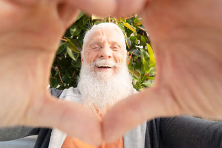 Smiling happy senior man with heart made of hands, happy retirement and charity conceptの写真素材