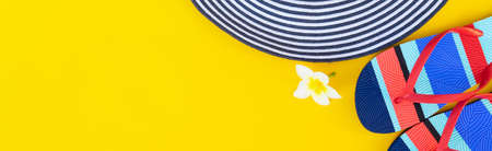 Summer flat lay scenery with hat, flip-flops sandals and flowers on bright yellow background with...