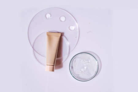 Glass petri dish with transparent pure serum for skin care with cosmetic tube on white background, top view. Concept laboratory tests and research, making and testing cosmeticの写真素材