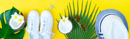 Summer flat lay boder with hat, shoes, coconuts and green leaves on yellow background with copy spaceの写真素材