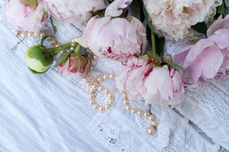 Fresh peonies flowers over lace background eith jewellery, top view, summer backgroundの写真素材