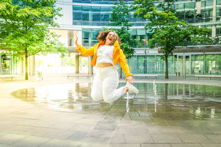 Happy curvy woman in city, plus size brunette lady with curly gray hair jumping emotionally in front...