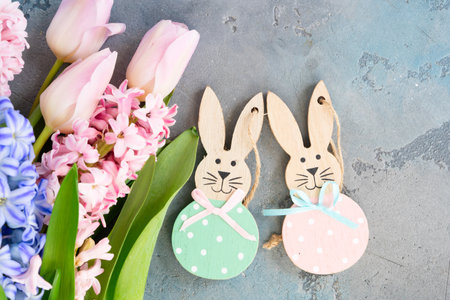 Easter scene with fresh tulips and hyacinth flowers and Easter bunnies over gray background