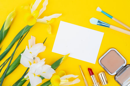 Minimal modern cosmetic scene with set of make up brushes, cosmetics and flowers set over yellow background, copy spaceの写真素材