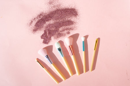 Minimal modern cosmetic scene with set of make up brushes set over pink background with glitter and shadow overlayの写真素材