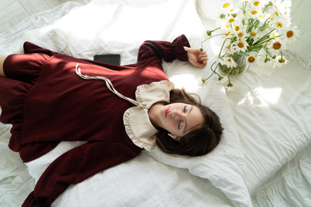 Teenager girl in headphones listening music in bed with flowersの写真素材