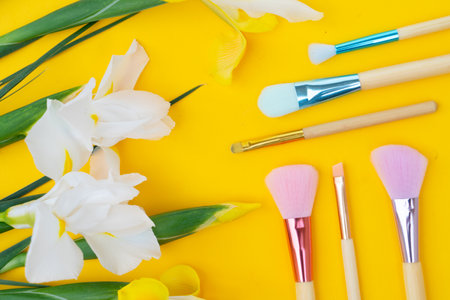Minimal modern cosmetic scene with set of make up brushes and flowers set over yellow backgroundの写真素材
