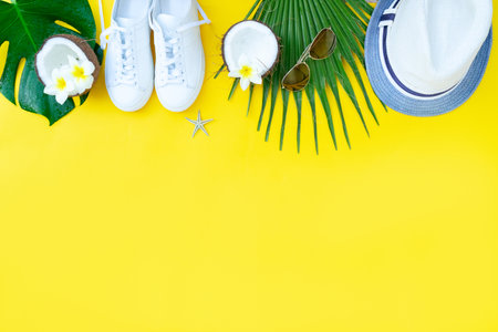 Summer flat lay boder with hat, shoes, coconuts and green leaves on yellow background with copy spaceの写真素材