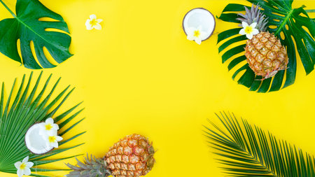 Summer flat lay frame with fresh tropical green leaves, coco and pineapples frame on yellow background bannerの写真素材