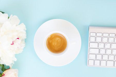 Flat lay home office workspace with cup of coffee, white modern keyboard and flowersの写真素材
