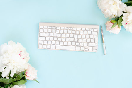 Flat lay home office workspace frame with white modern keyboard and peony flowersの写真素材