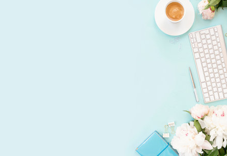 Flat lay home office workspace background with white modern keyboard, notebook and peony flowers, copy space on blue backgroundの写真素材