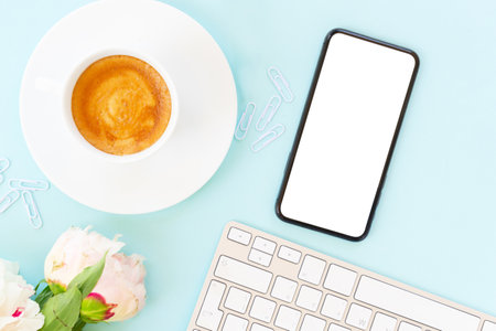Home office desktop with peony flowers and modern phone on blueの写真素材