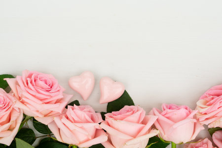 Rose fresh flowers border with two Valentines day hearts on light table from above with copy space, flat lay sceneの写真素材