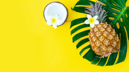 Summer flat lay scene with tropical green leaves, coco and pineapple, copy space on yellow background bannerの写真素材