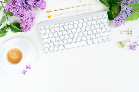 Flat lay top view home office workspace - modern keyboard with cup of coffee and lilac flowers on white backgroundの写真素材