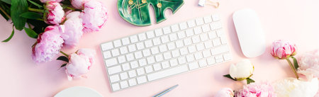 Flat lay home office workspace - modern white keyboard with cup of coffee and peony flowers, copy space on pink backgroundの写真素材
