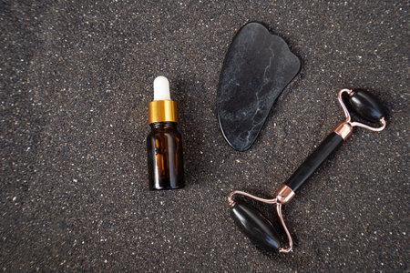 gua sha, face massage roller made of natural stone over black sand backgroundの写真素材