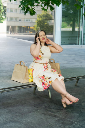 Happy curvy woman with ecological shopping bags sitting and talking on mobile phone enjoying in shopping. Consumerism, shopping, lifestyle conceptの写真素材