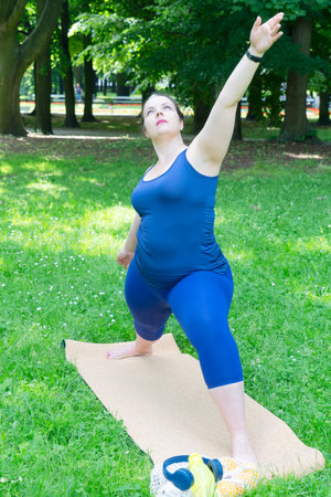 Woman and sports, exercise for weight loss in the fresh air. Happy curvy 40s woman doing workout stretch routine outdoor at green city parkの写真素材