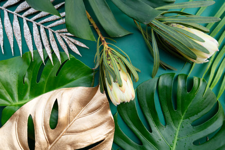 Tropical leaves and flowers over green background, summer background, top viewの写真素材