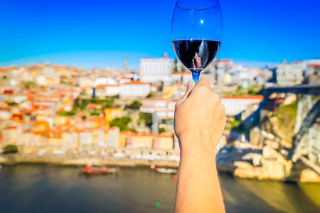 hand of woman with glass of ruby port wine on historic town of Porto, background Portugalの写真素材