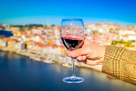 hand of woman with glass of ruby port wine on historic town of Porto, background Portugalの写真素材