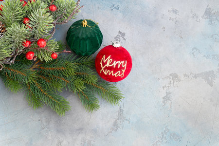 red bauble with Merry Xmas script nestled among frosty pine branches and pinecone, textured blue-gray backdrop and warm tones create nostalgic seasonal sceneの写真素材