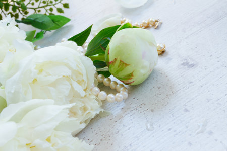 White fresh peony flowers and buds with pearls jewellery on aged white wooden table with copy spaceの写真素材