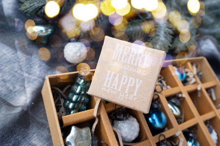 Box of vintage Christmas ornaments in green and blue on silver fabric backdrop, ready for holiday...