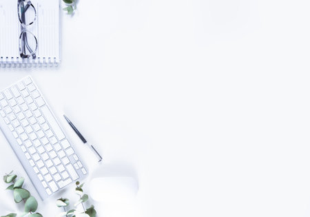 Flat lay home office workspace with white modern keyboard, notebook and green twigsの写真素材