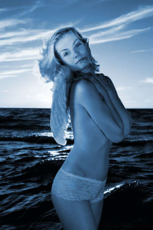 Angel girl in a sea at sunset time (toned in blue)の写真素材