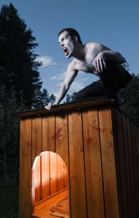 Scary man sitting on kennel and turning into werewolfの写真素材