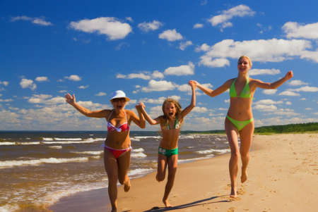 Mother and two daughters running on a beach near the waterの写真素材