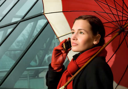 Beautiful brunette with red umbrella talking on the phoneの写真素材