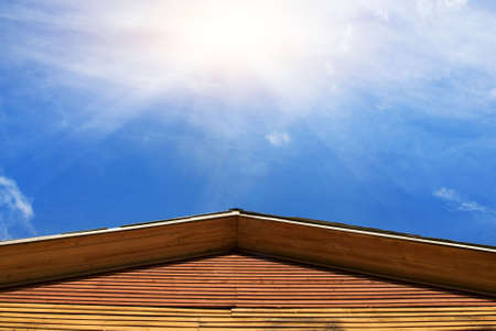Bulding's roof and blue sky with a sun behind itの写真素材