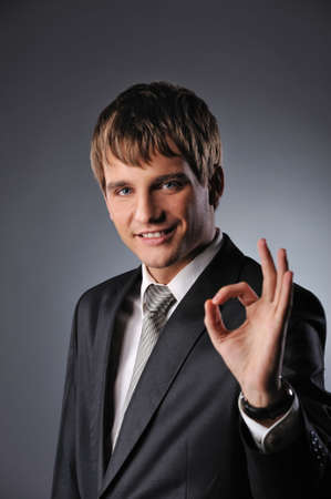 Cheerful businessman showing OK sign over grey backgroundの写真素材