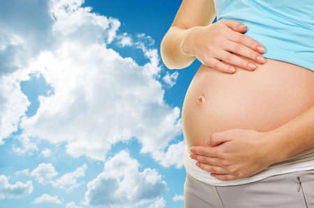 Beautiful pregnant belly over blue cloudy skyの写真素材