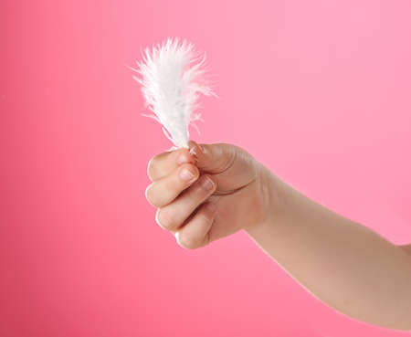 Child's hand holding white feather. Isolated on pink backgroundの写真素材